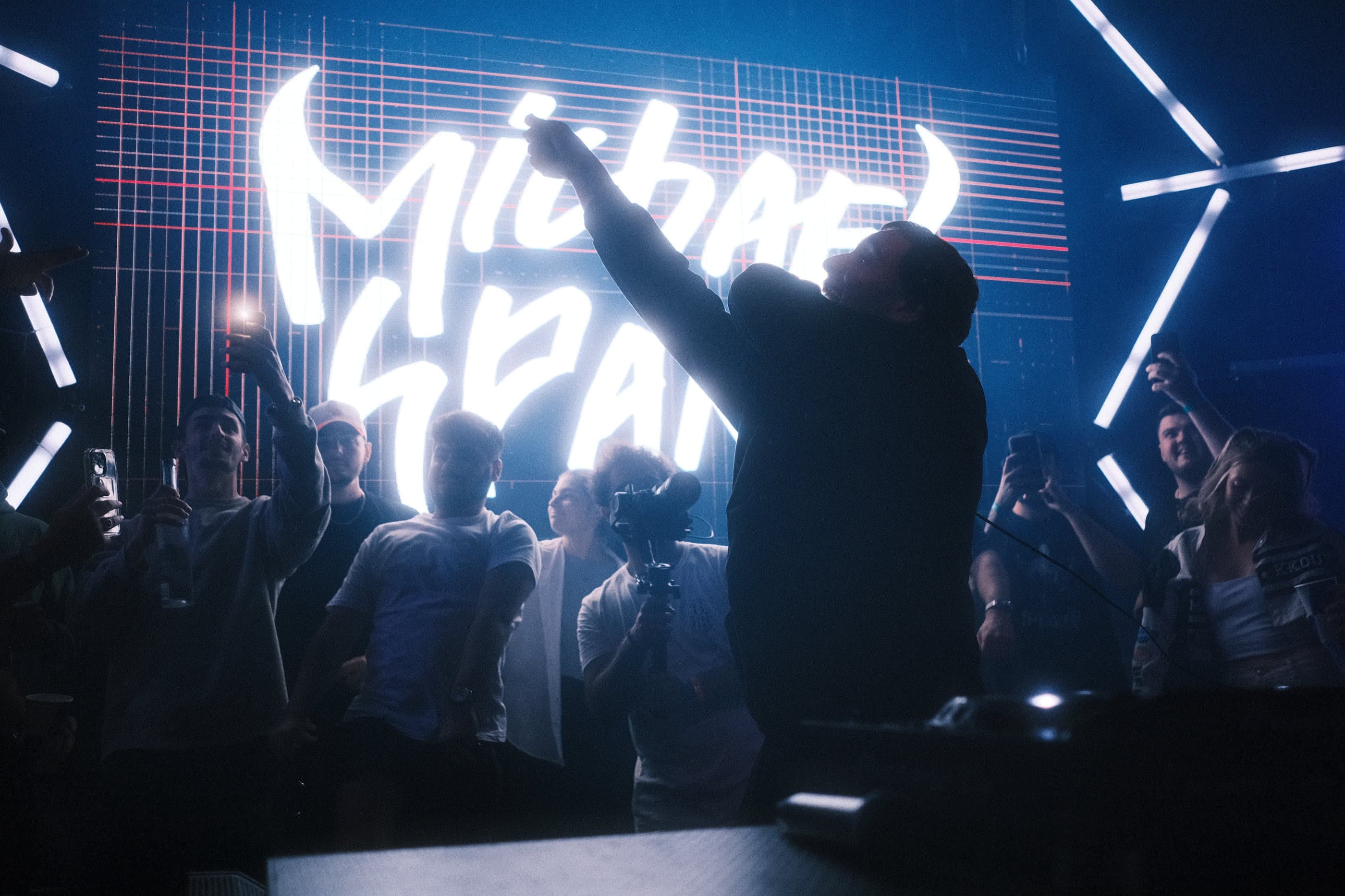 Artist silhouetted against a glowing neon sign, crowd cheering