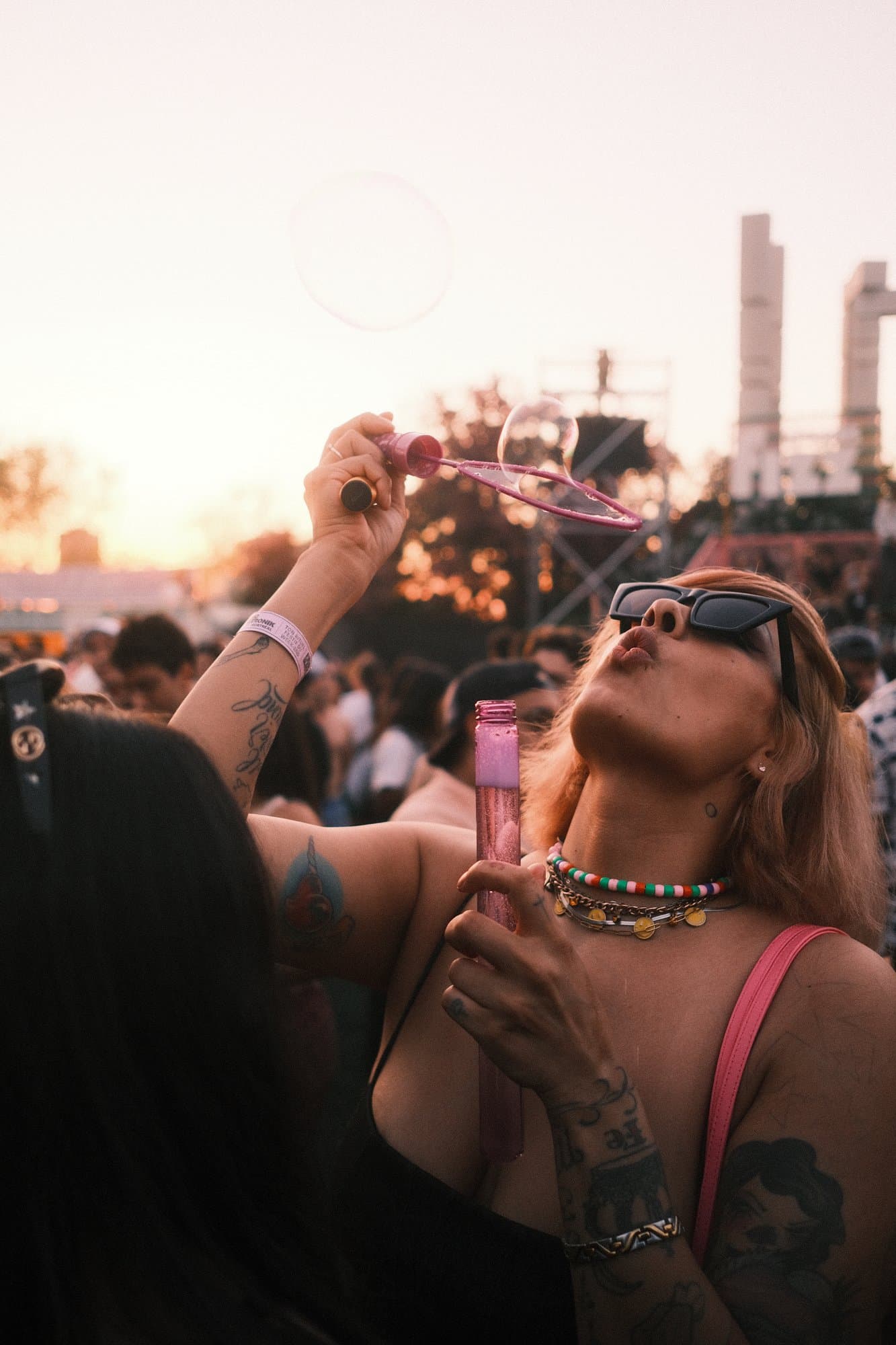 A woman blowing bubbles at golden hour in a festival crowd