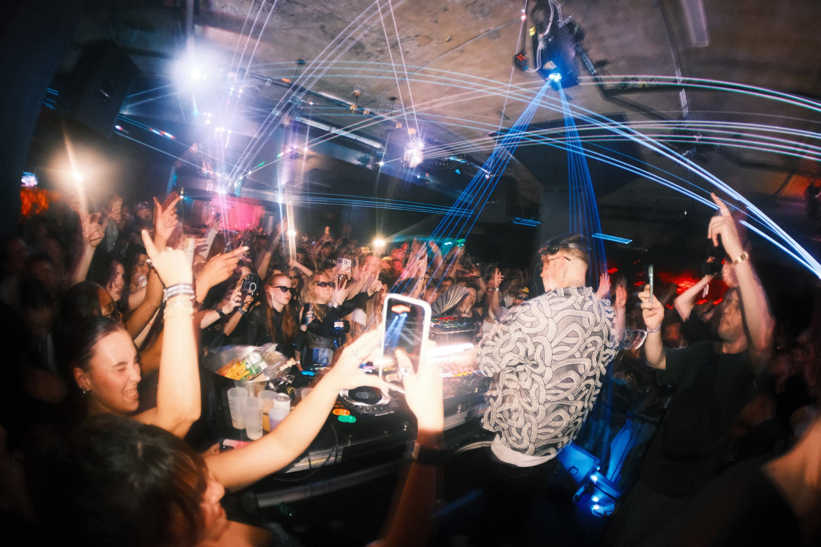 DJ booth lit by blue laser trails in a packed club