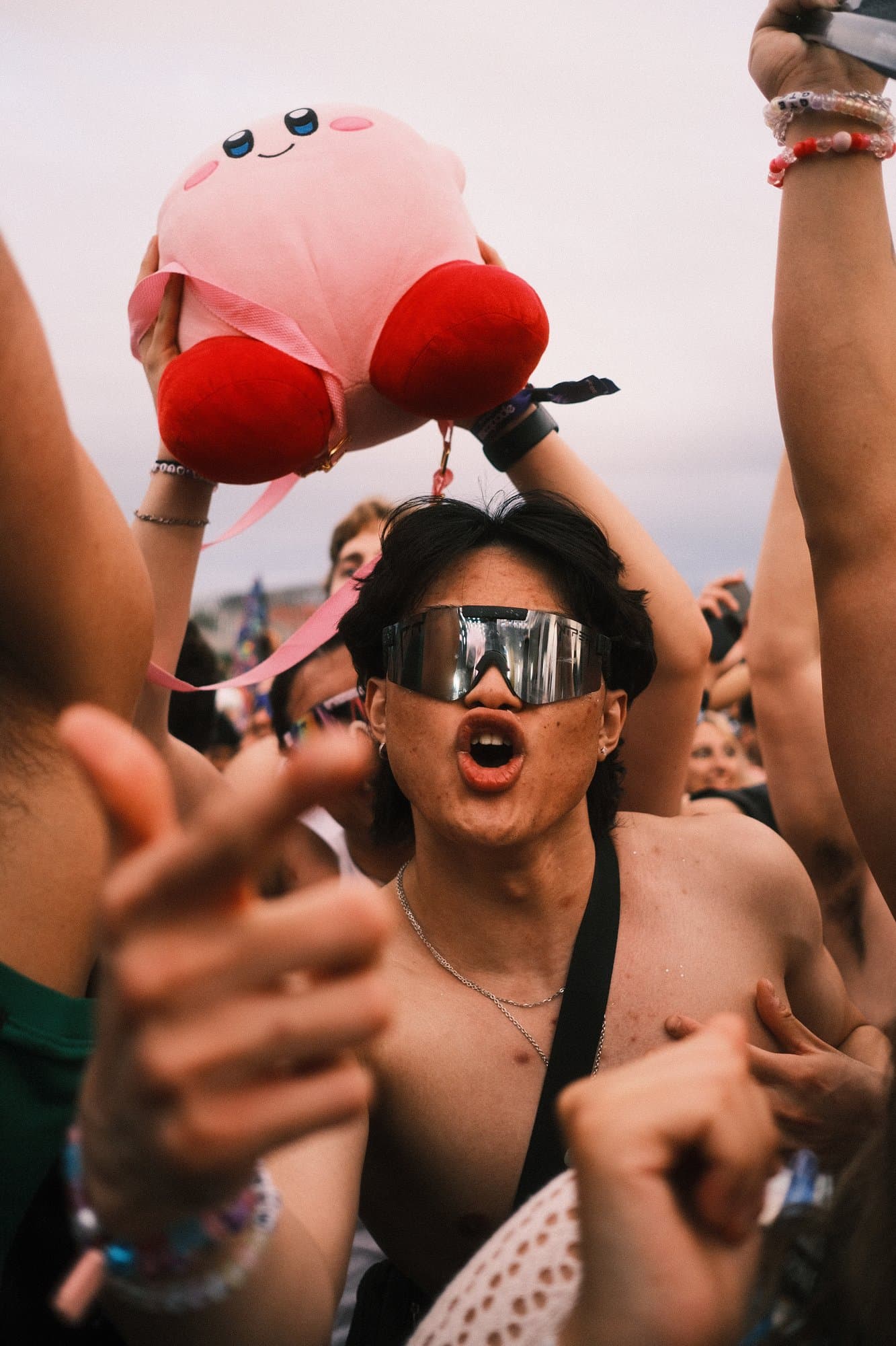 A festival-goer holding up a Kirby plush, mirrored sunglasses reflecting the crowd
