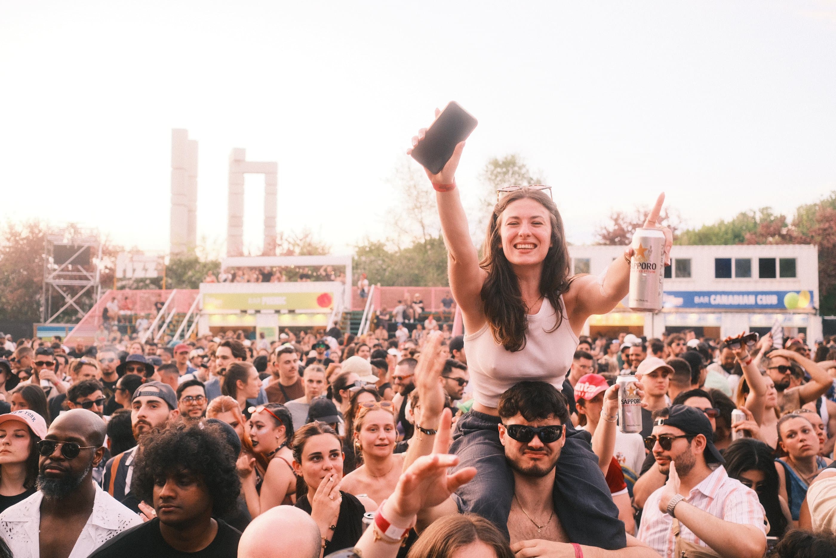 A woman cheering on someone's shoulders in a festival crowd at golden hour