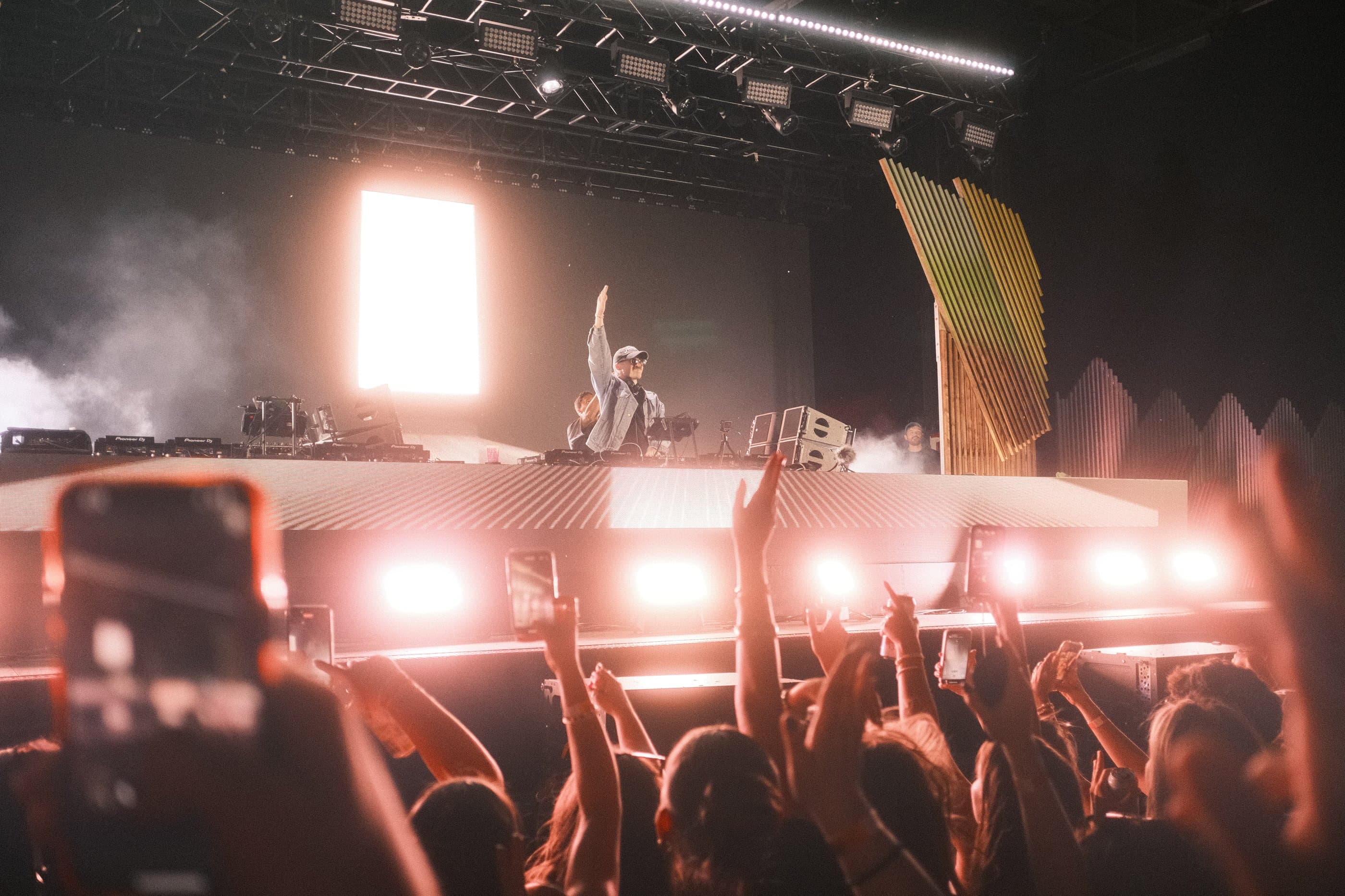 Artist silhouetted on stage under warm light, phones raised in the crowd below